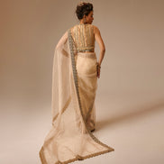 Woman wearing a beige saree with a gold blouse against a beige background
