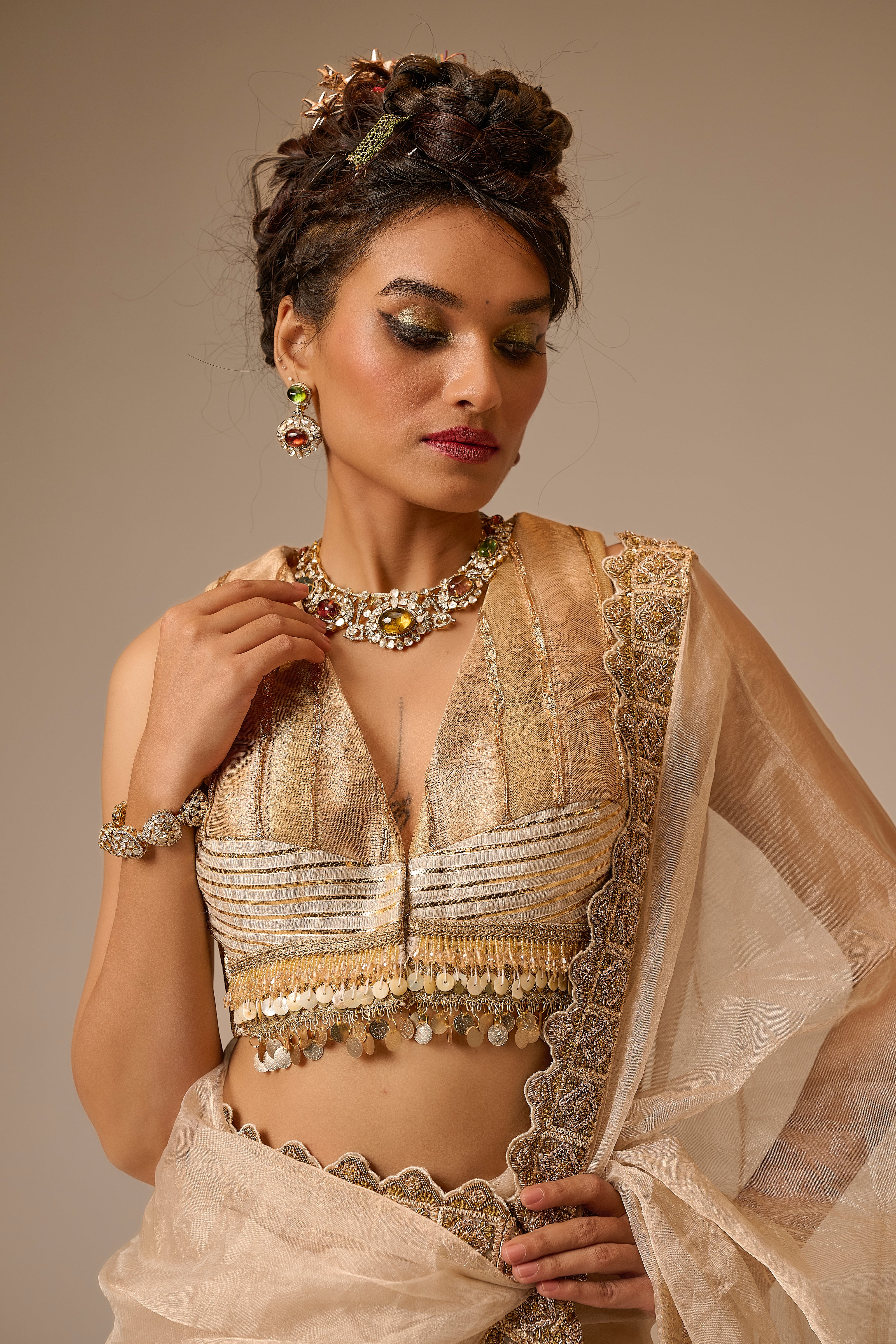 Woman in traditional beige and gold outfit with jewelry against a neutral background