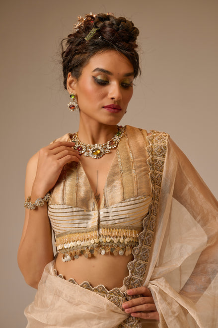Woman in traditional beige and gold outfit with jewelry against a neutral background