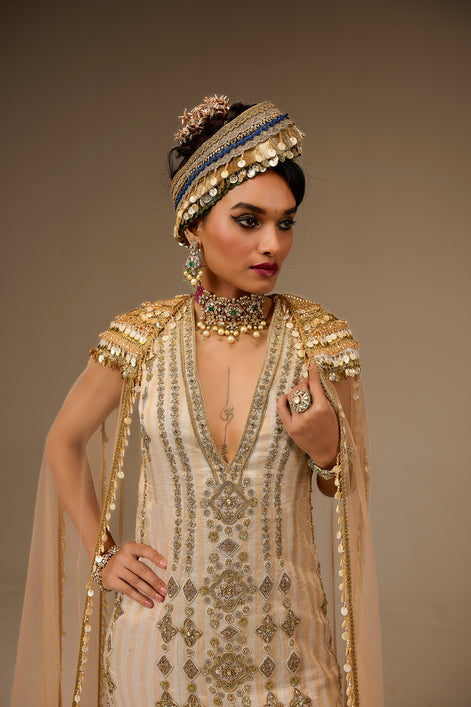 Woman in an ornate, beaded outfit with a matching headpiece against a neutral background