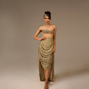 Woman wearing a gold dress with intricate detailing on a plain background