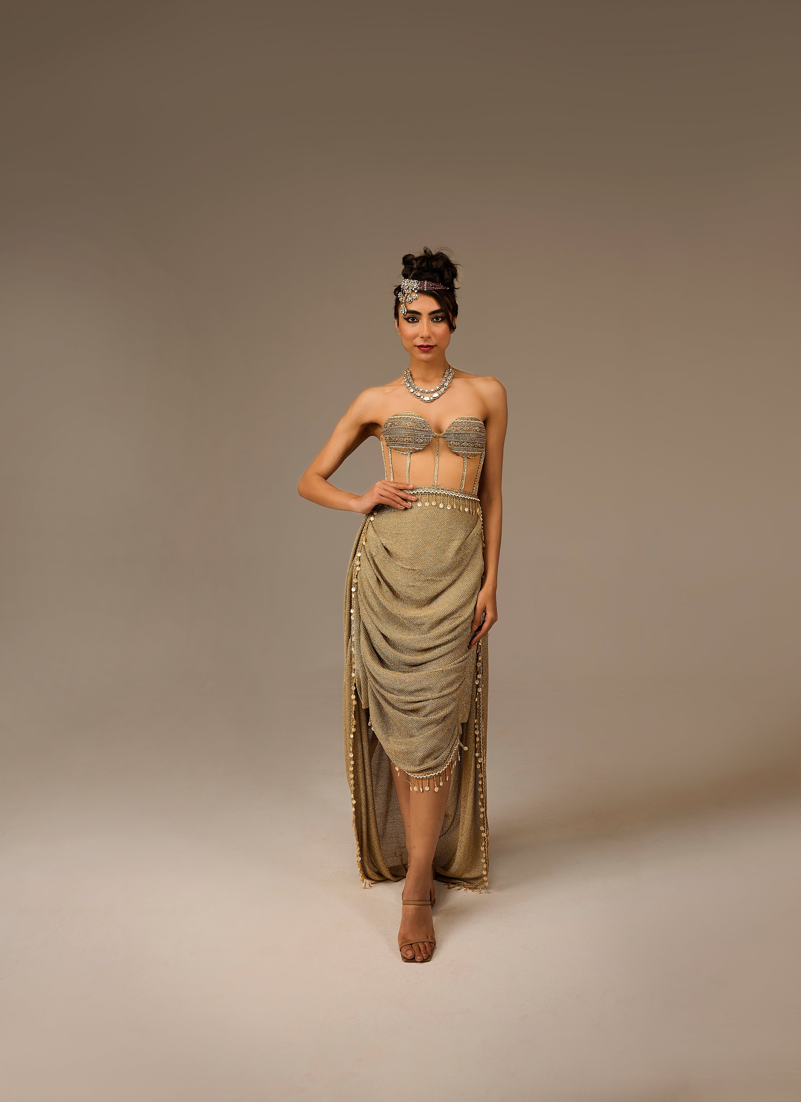 Woman wearing a gold dress with intricate detailing on a plain background