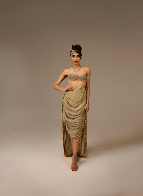 Woman wearing a gold dress with intricate detailing on a plain background