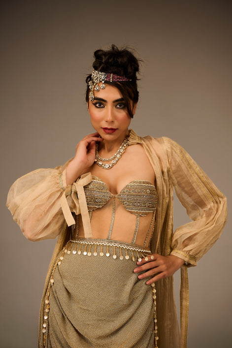 Woman in a gold and beige traditional outfit with jewelry against a brown background