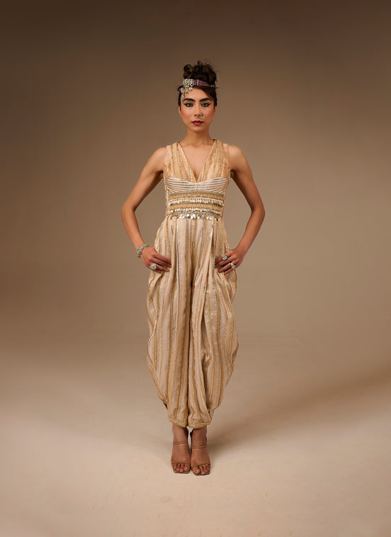 Woman wearing a beige and gold dress with a headpiece against a brown background