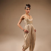 Woman wearing a gold and beige outfit with a headpiece against a brown background