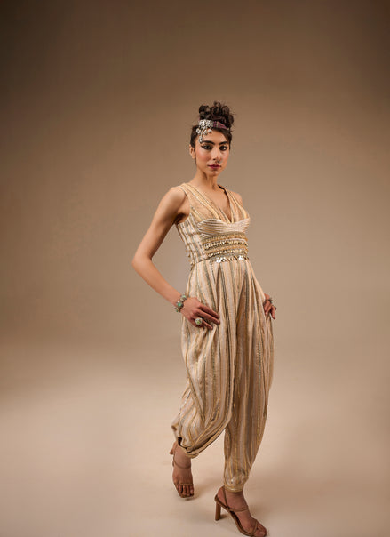 Woman wearing a gold and beige outfit with a headpiece against a brown background