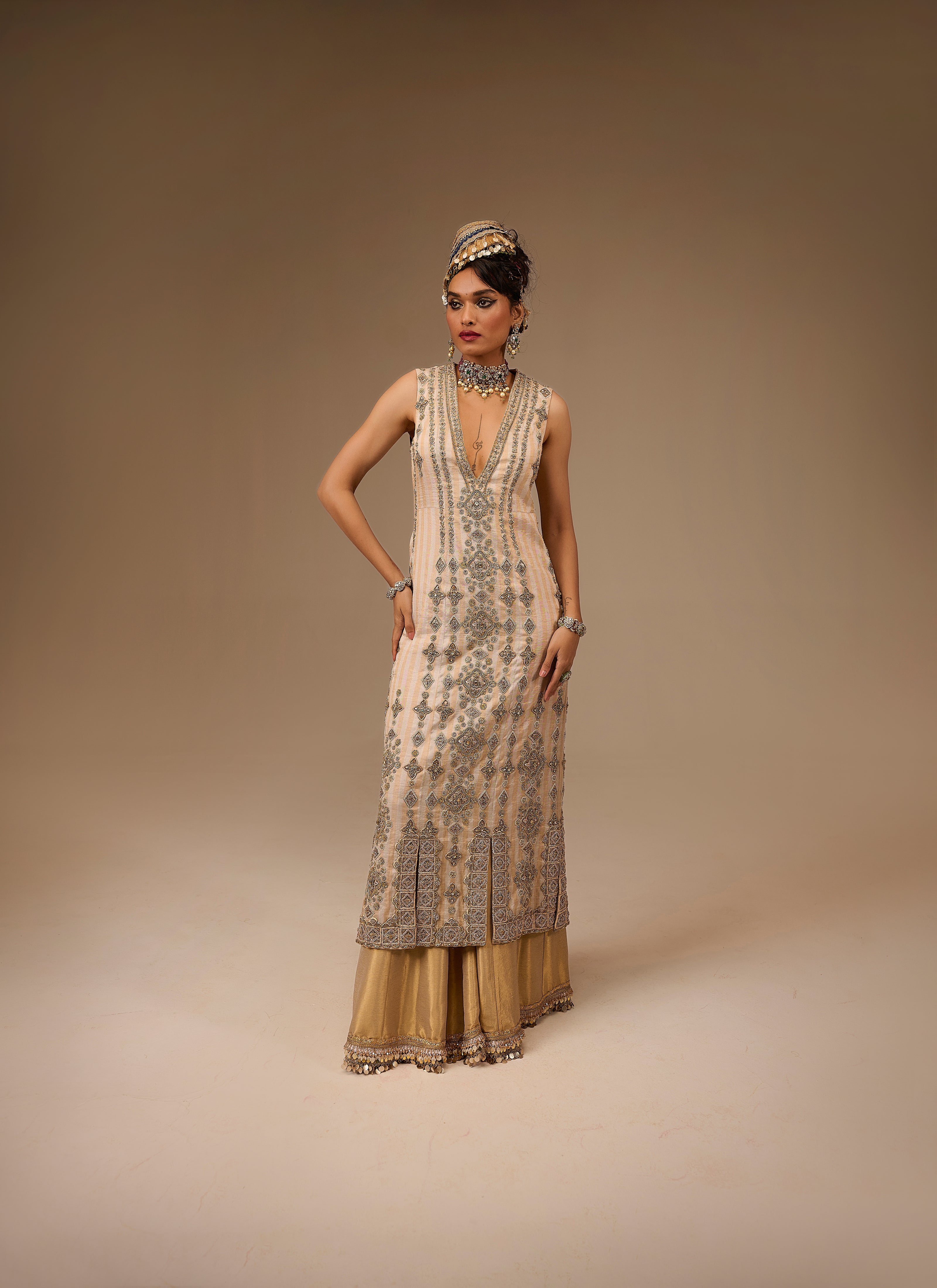 Woman wearing a long, ornate dress with intricate patterns on a beige background
