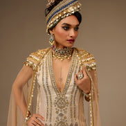 Woman in an ornate, beaded outfit with a matching headpiece against a neutral background