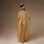 Woman wearing a gold evening gown with a hat on a plain background