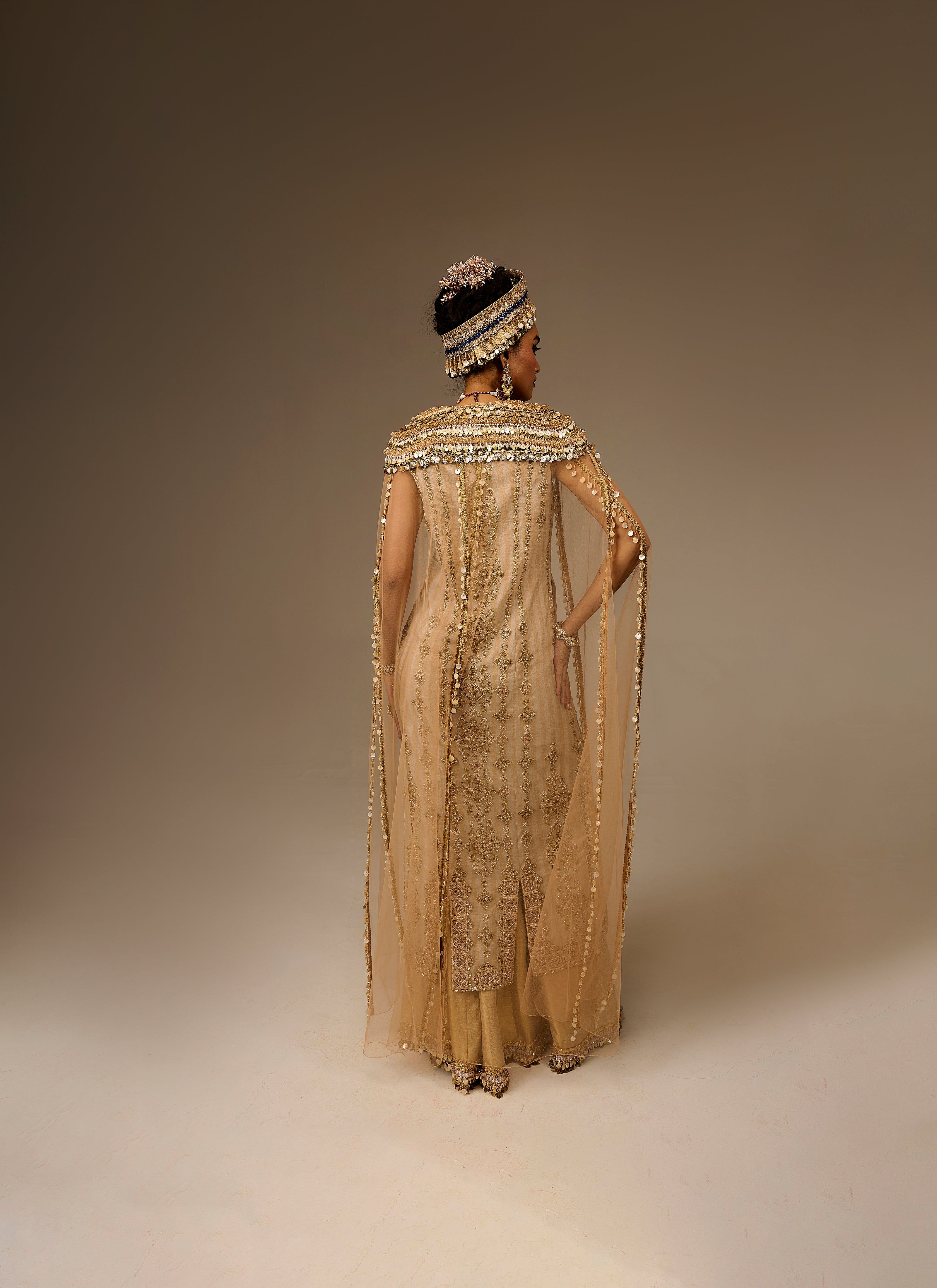 Woman wearing a gold evening gown with a hat on a plain background