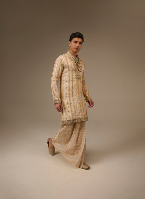Man wearing a traditional beige kurta with pants on a plain background