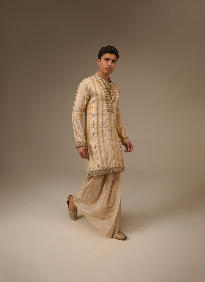 Man wearing a traditional beige kurta with pants on a plain background