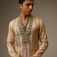 Man wearing a traditional embroidered kurta with intricate designs on a plain background