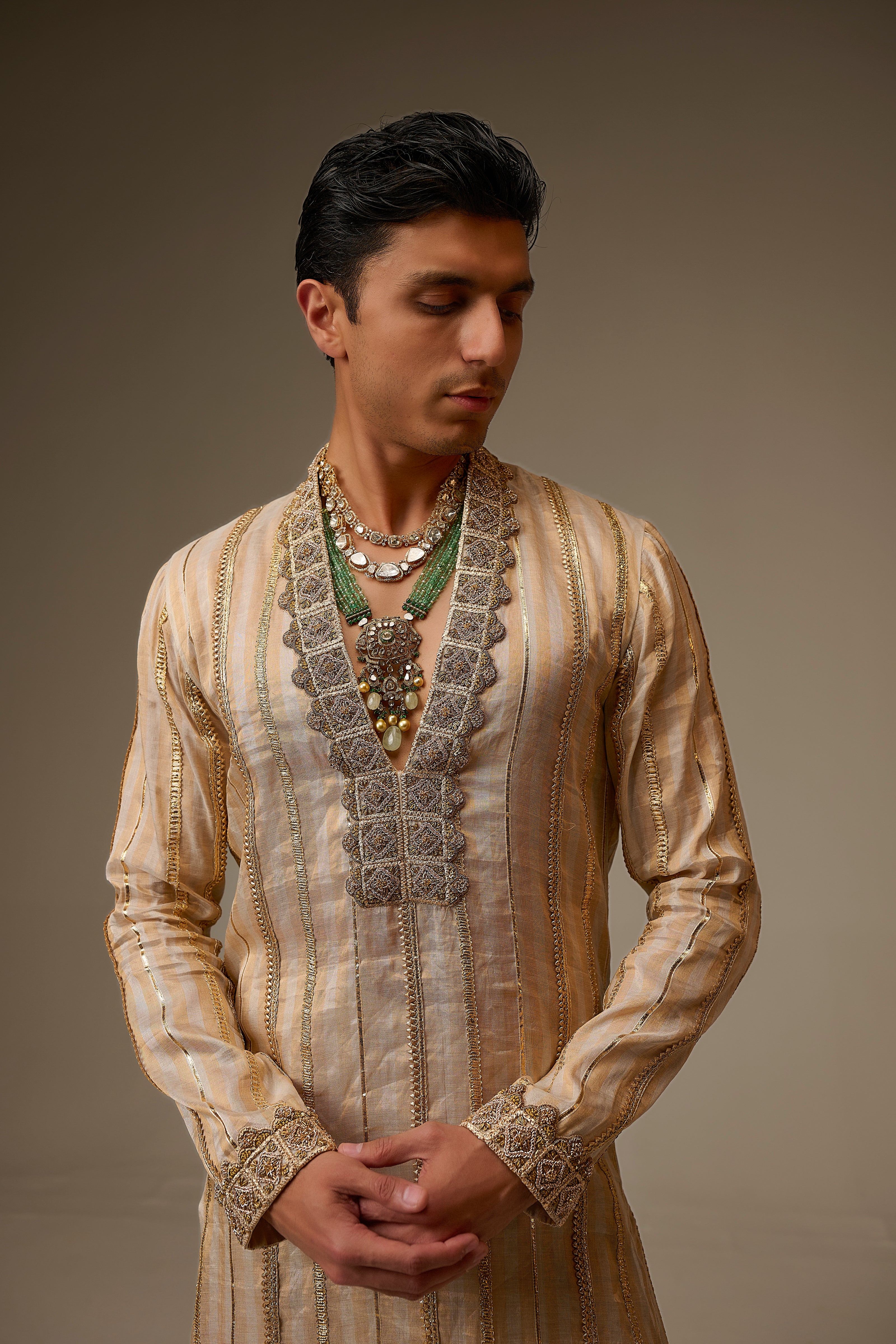Man wearing a traditional embroidered kurta with intricate designs on a plain background