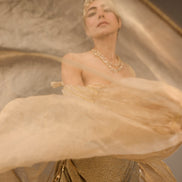 Woman in a gold dress with a sheer overlay, standing against a neutral background.