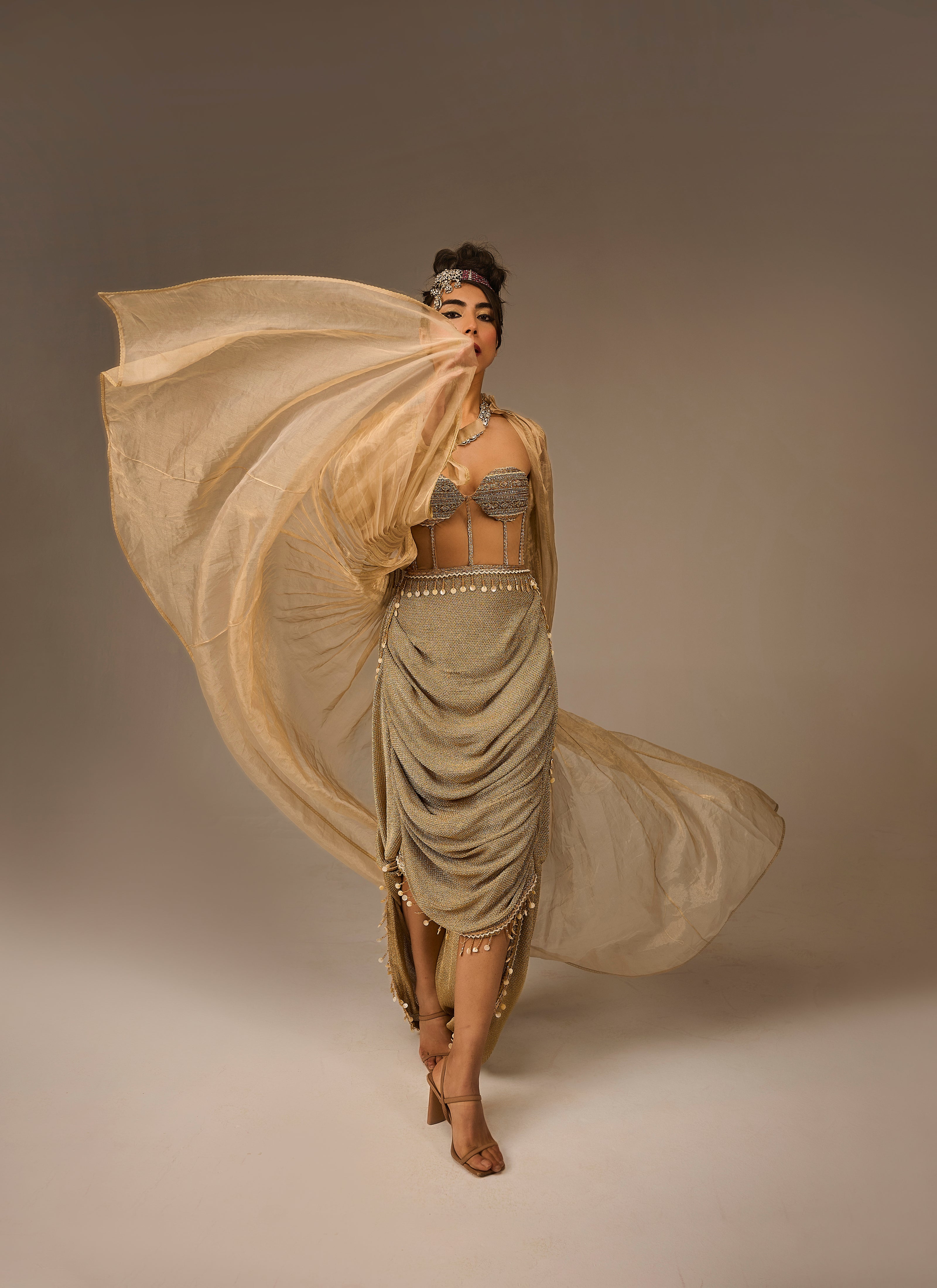Woman in a flowing beige dress against a plain background