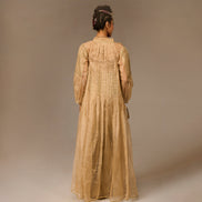 Woman wearing a long beige dress against a plain background