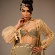Woman in a gold and beige traditional outfit with jewelry against a brown background