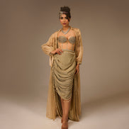 Woman in a flowing beige dress with intricate detailing on a plain background