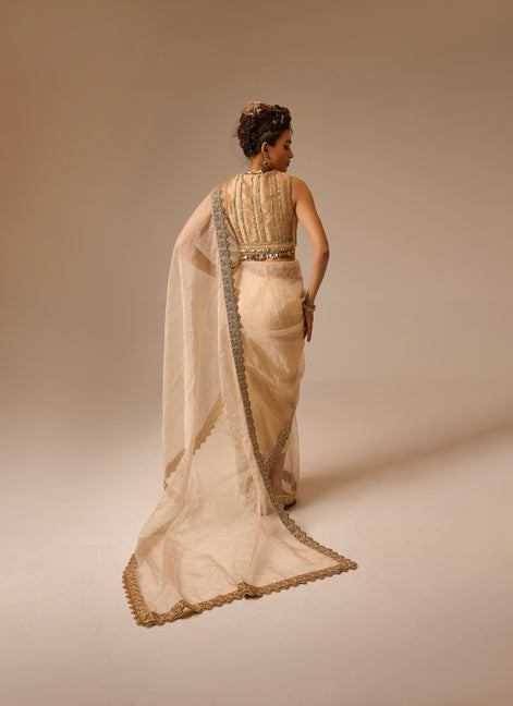 Woman wearing a beige saree with a gold blouse against a beige background