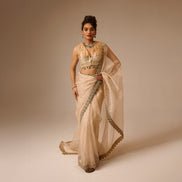 Woman wearing a beige saree with intricate designs on a beige background