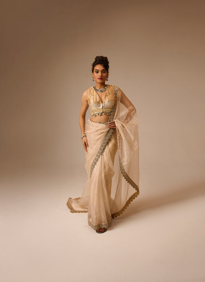 Woman wearing a beige saree with intricate designs on a beige background