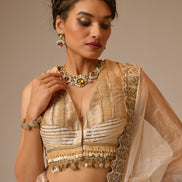 Woman in traditional beige and gold outfit with jewelry against a neutral background
