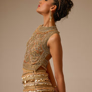 Woman wearing an ornate, gold embroidered outfit against a beige background