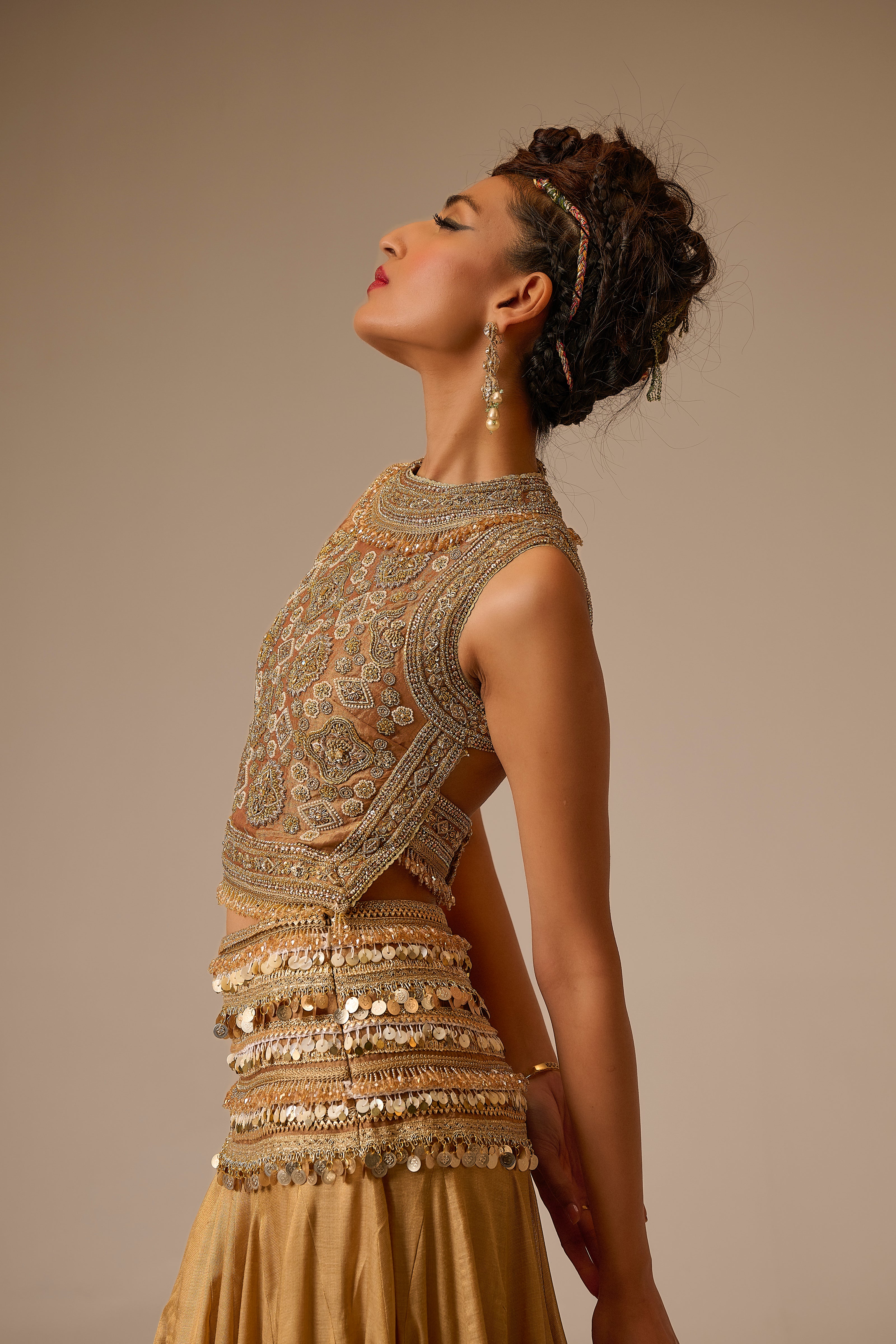 Woman wearing an ornate, gold embroidered outfit against a beige background