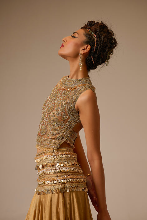Woman wearing an ornate, gold embroidered outfit against a beige background