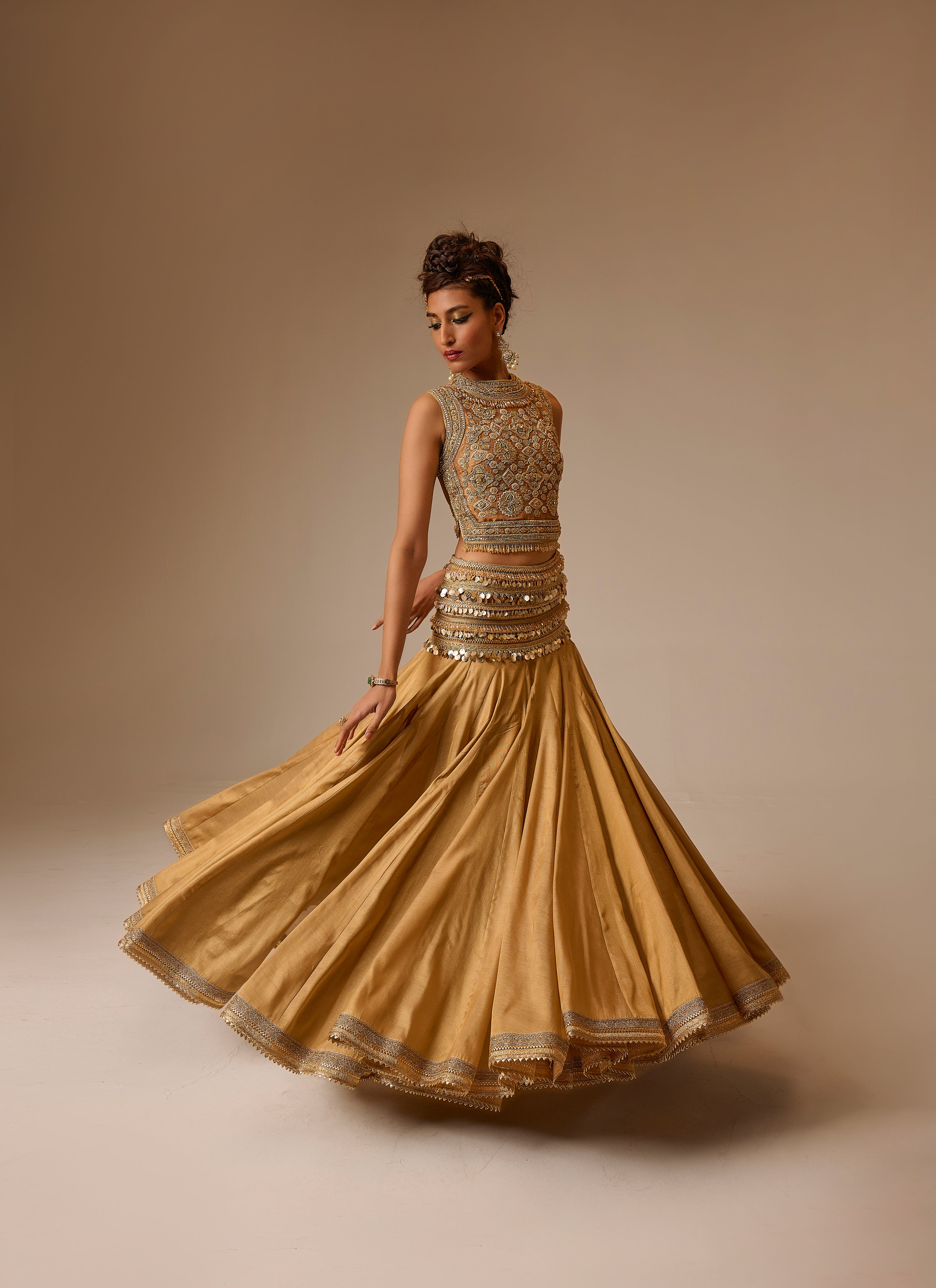 Woman wearing a gold traditional outfit with intricate designs on a beige background