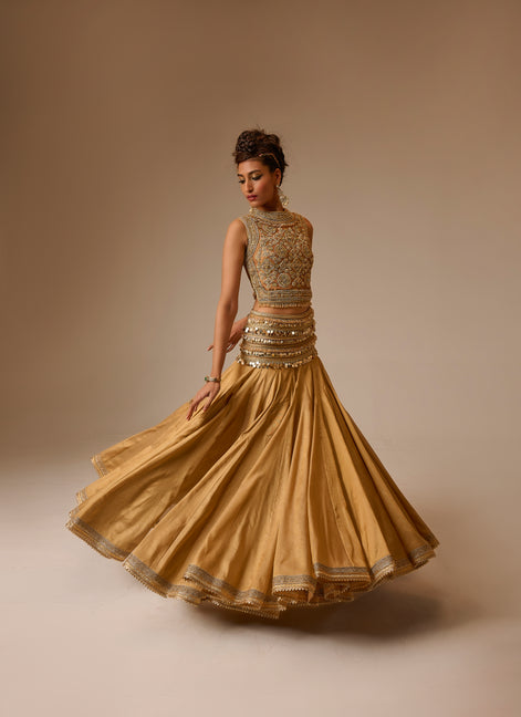 Woman wearing a gold traditional outfit with intricate designs on a beige background