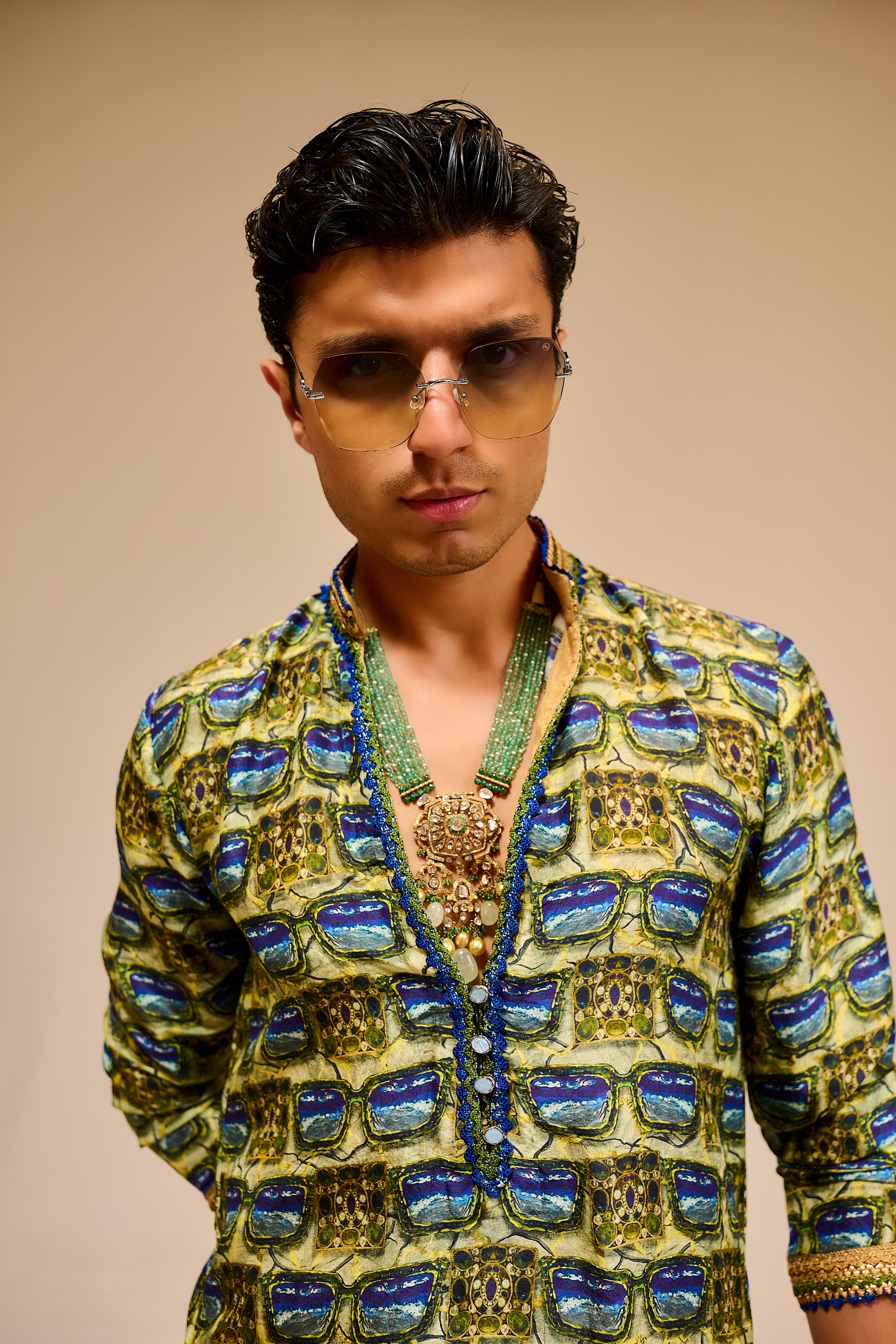 Man wearing a patterned jacket and sunglasses against a beige background