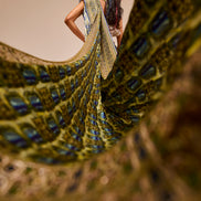 Woman in a colorful saree standing behind a peacock with a blurred background