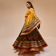Woman wearing a traditional multicolored and patterned dress with a yellow dupatta on a beige background