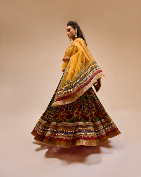 Woman wearing a traditional multicolored and patterned dress with a yellow dupatta on a beige background