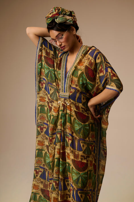Woman wearing a colorful patterned dress and headscarf against a neutral background