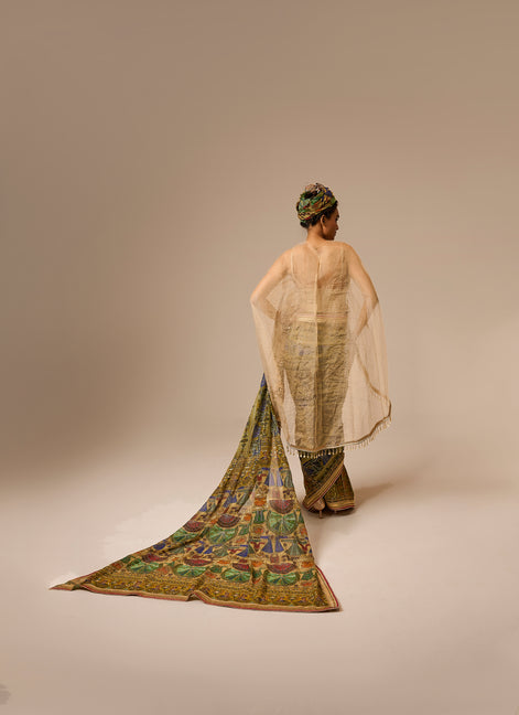 Woman wearing a traditional outfit with a long, colorful scarf on a plain background
