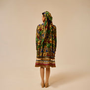 Person wearing a colorful patterned dress and headscarf on a beige background