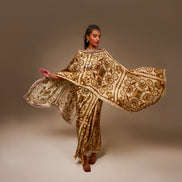 Woman wearing a gold and brown embroidered traditional outfit against a plain background
