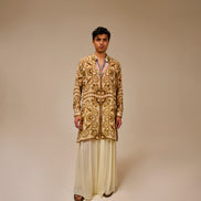 Man wearing a patterned kurta with white pants on a beige background