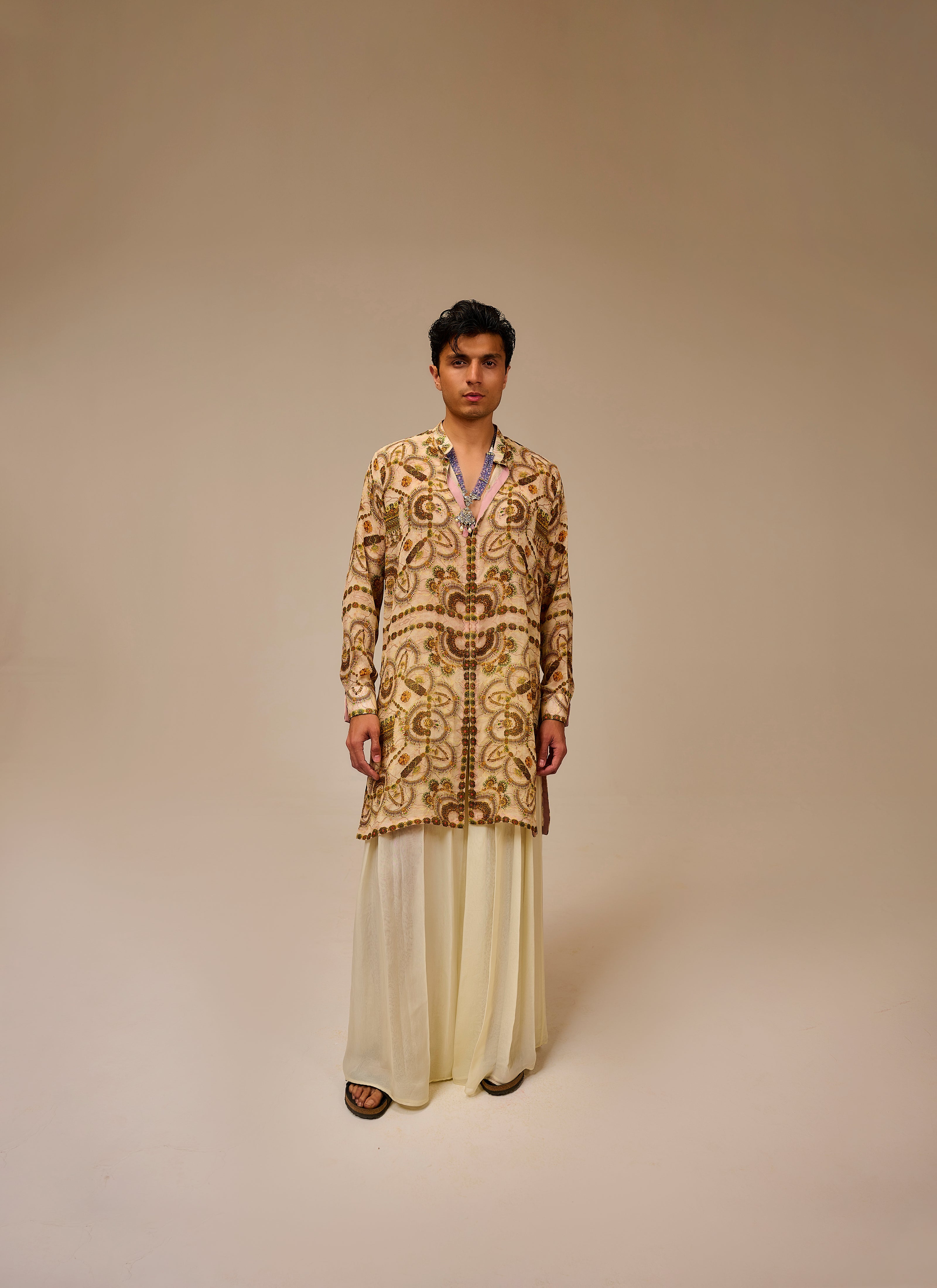 Man wearing a patterned kurta with white pants on a beige background