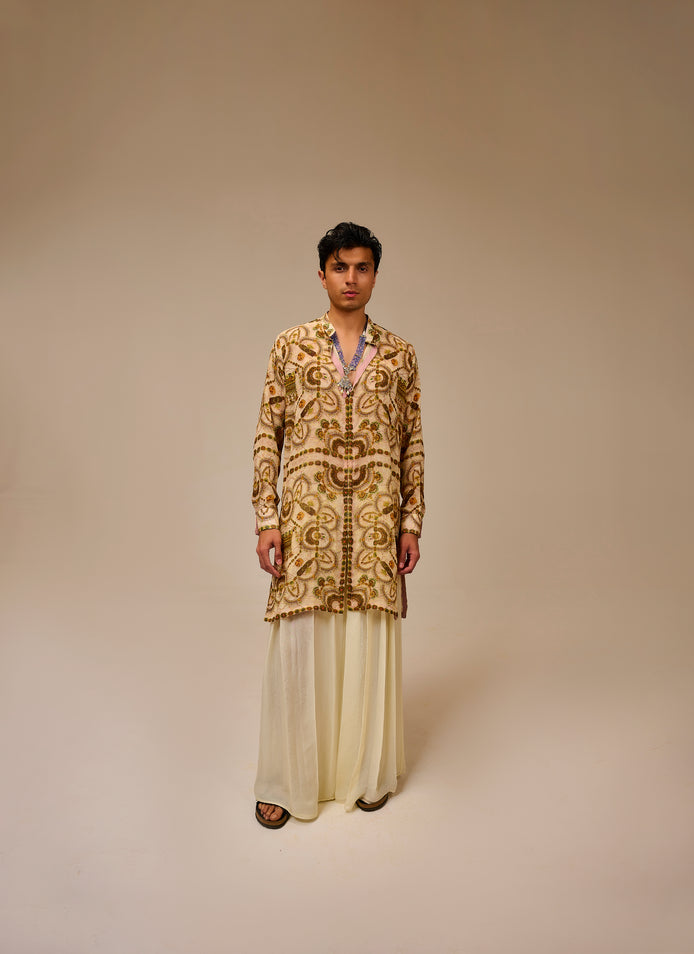 Man wearing a patterned kurta with white pants on a beige background