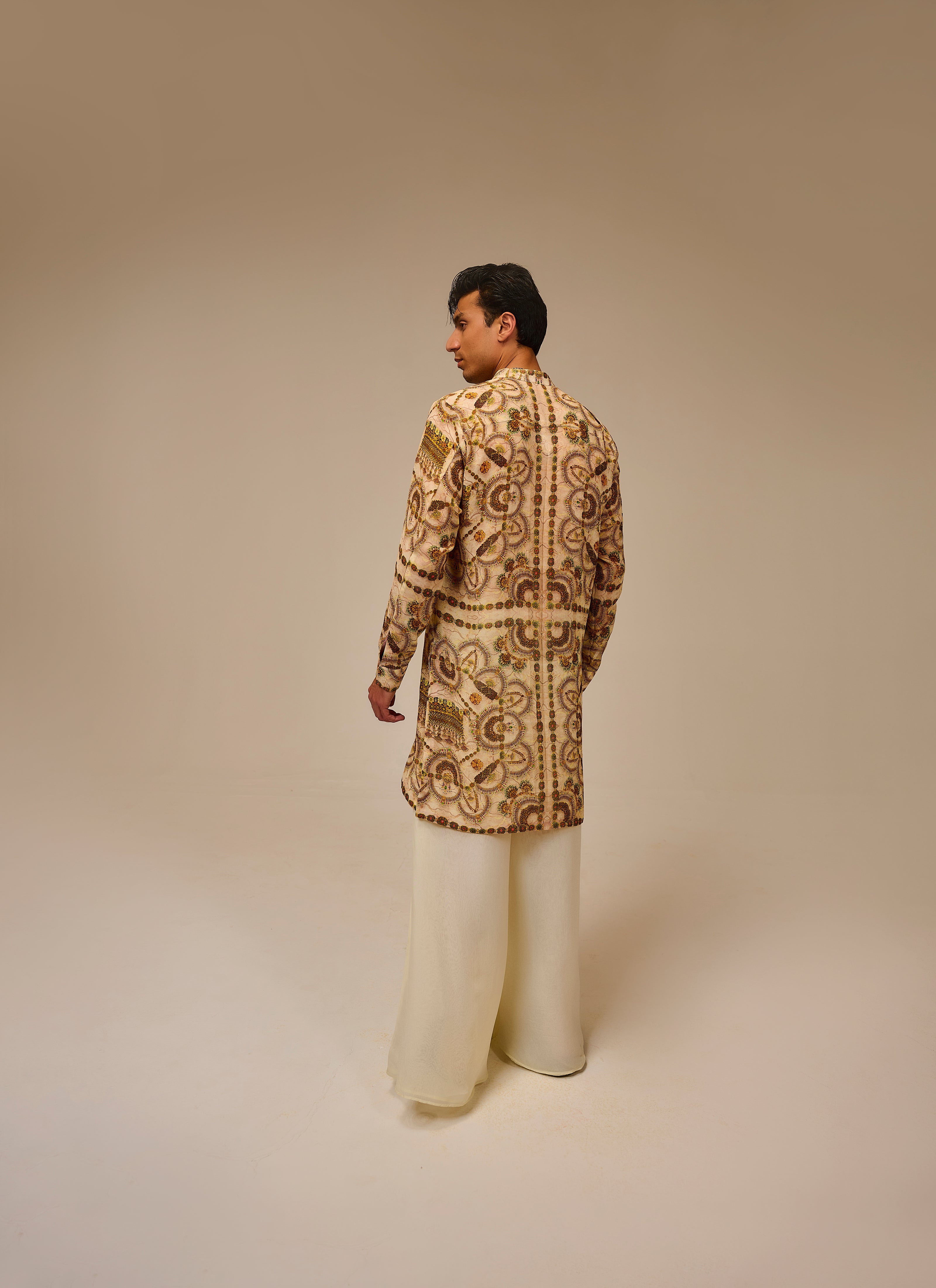 Man wearing a patterned jacket and white pants on a beige background