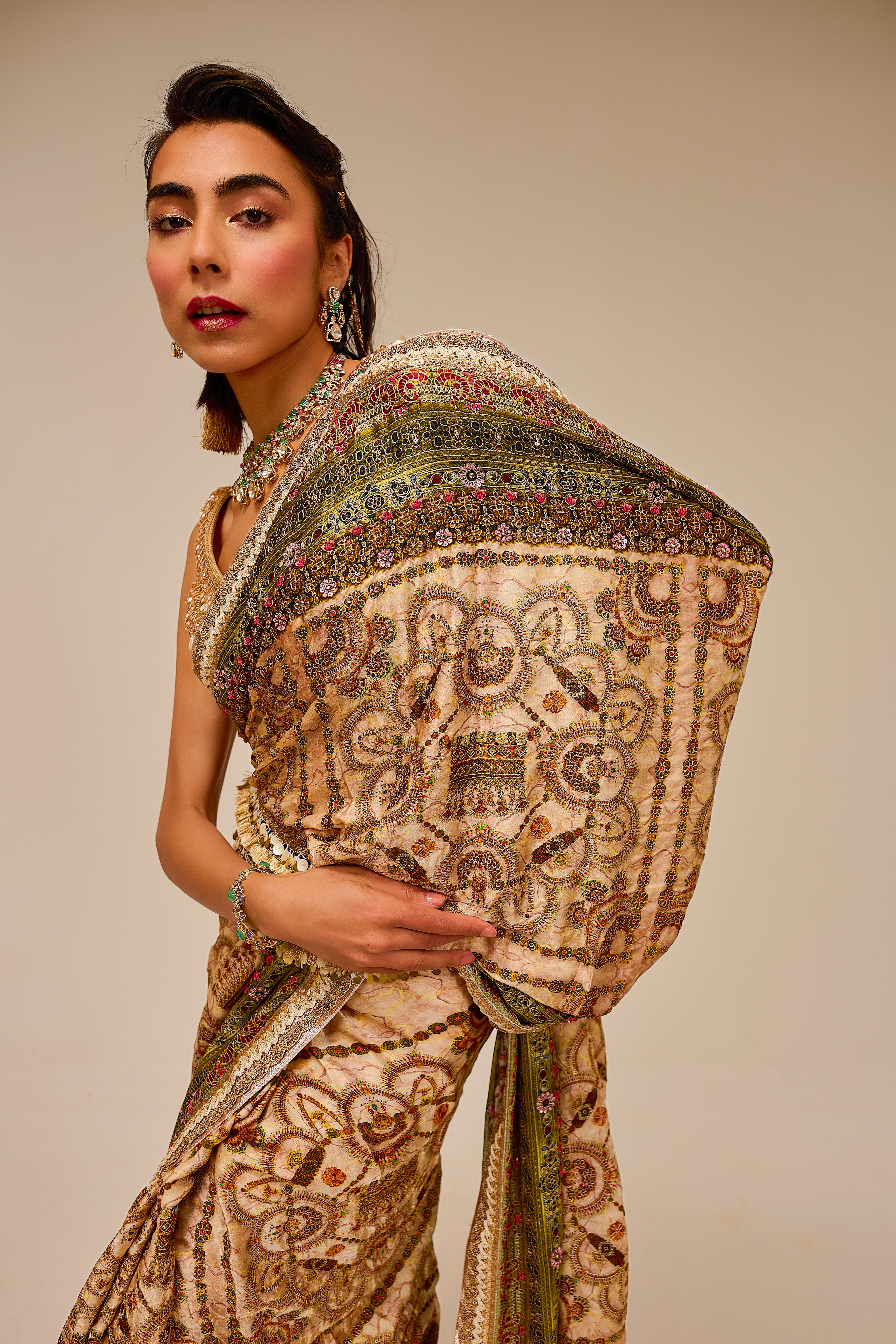 Woman wearing a traditional embroidered saree against a beige background