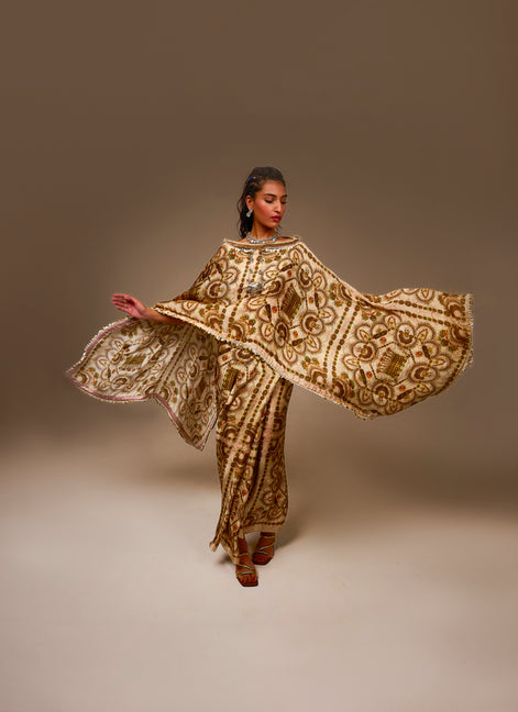 Woman wearing a gold and brown embroidered traditional outfit against a plain background