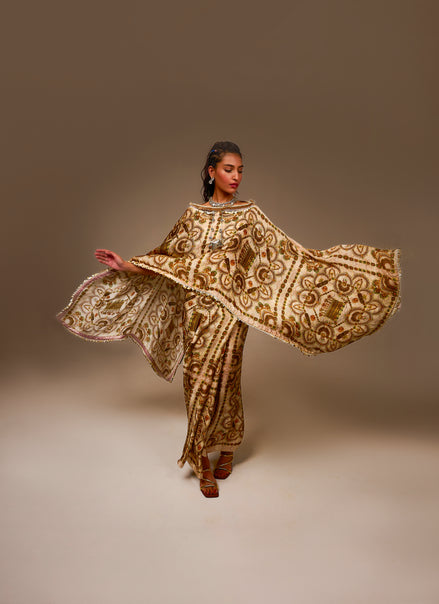 Woman wearing a gold and brown embroidered traditional outfit against a plain background