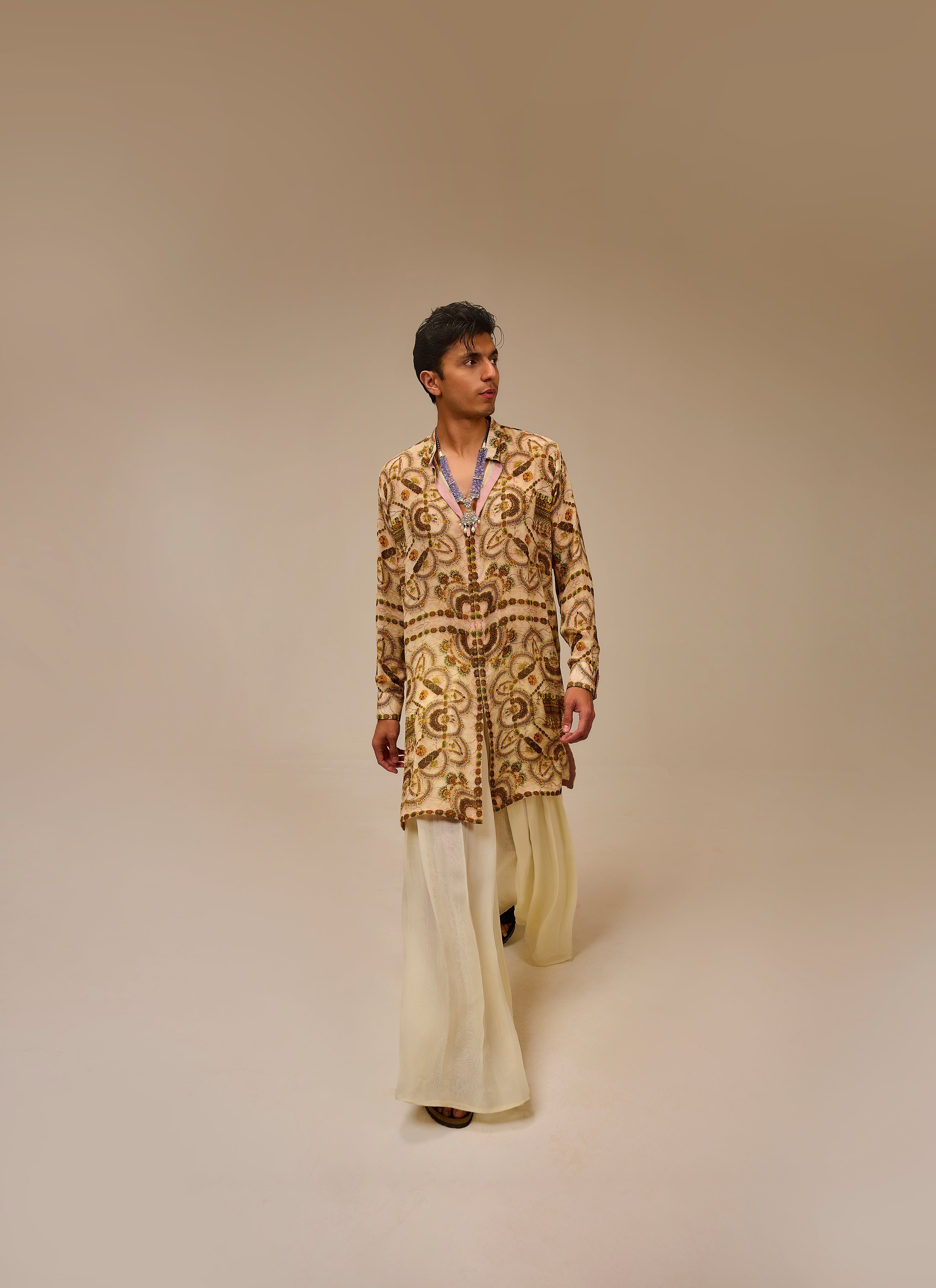 Man wearing a patterned jacket and light-colored pants on a beige background