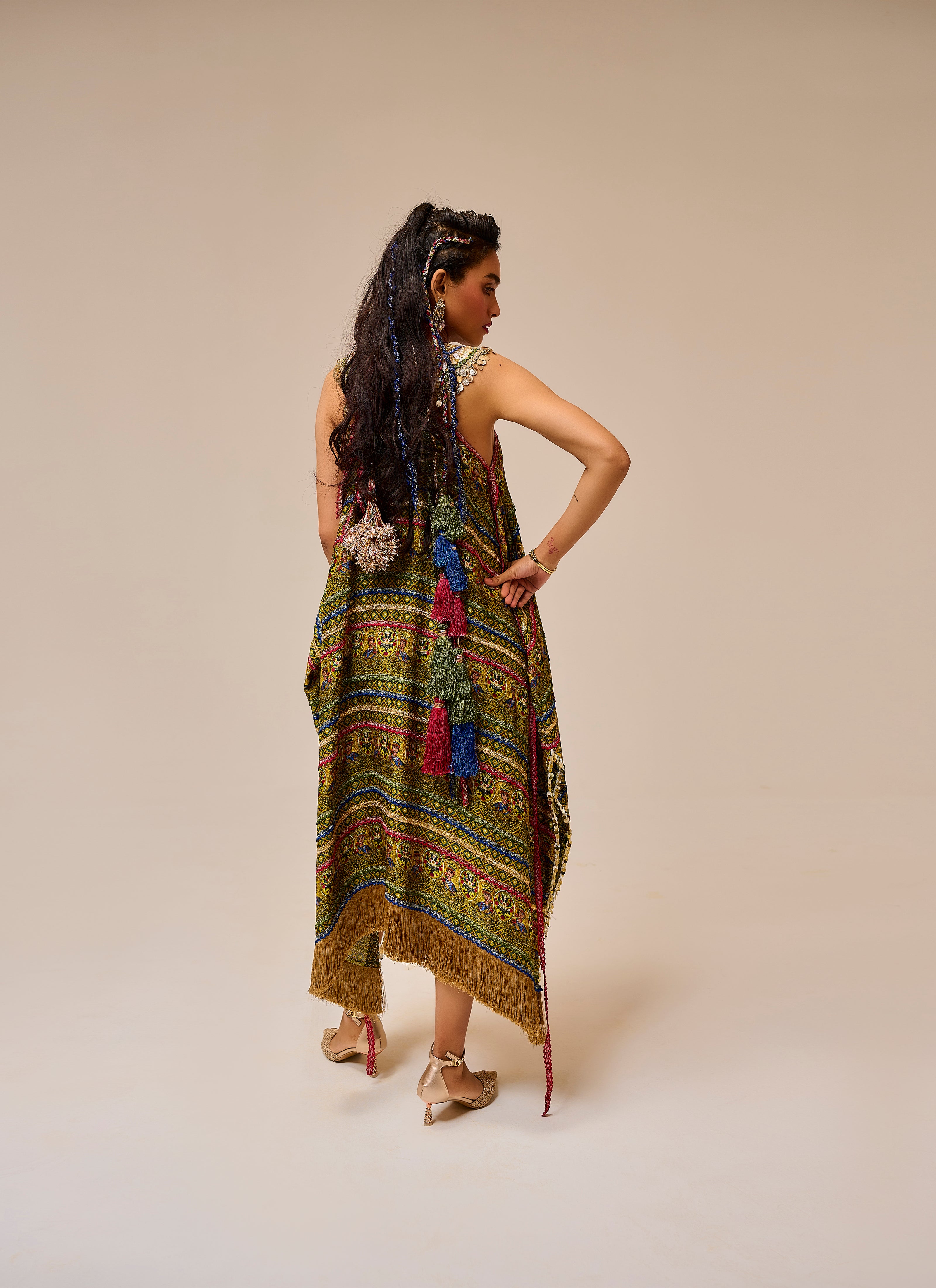 Woman wearing a colorful patterned dress with fringe on a beige background